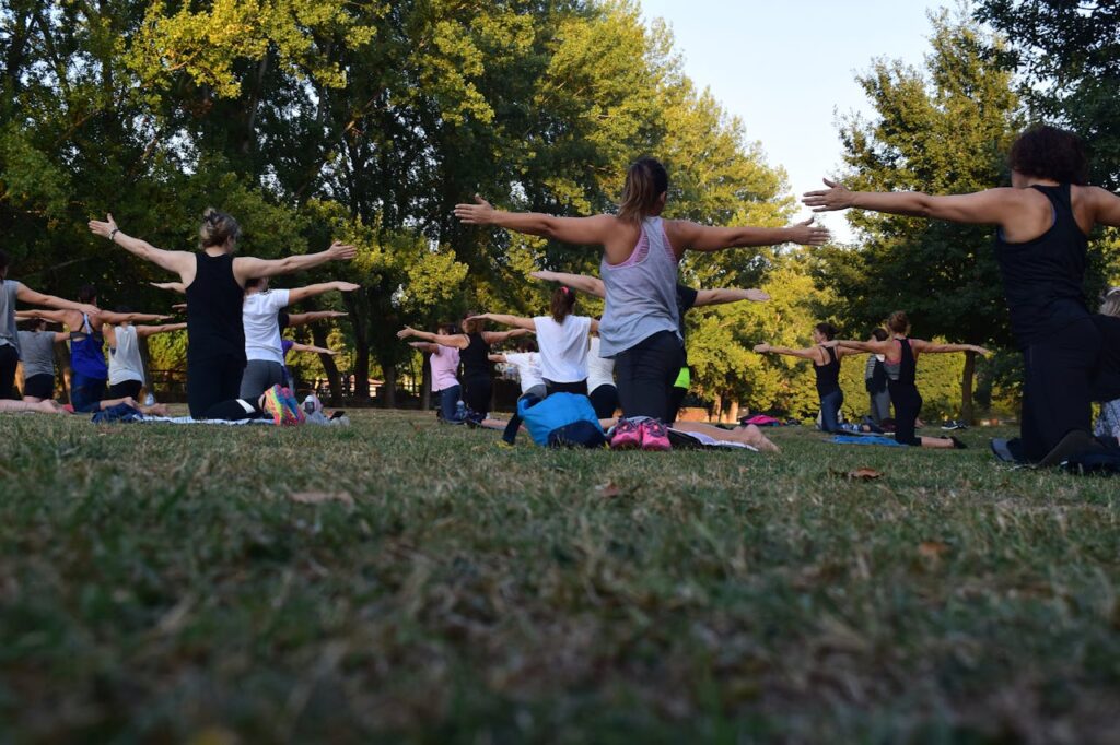 pexels-photo-1472887 Group of adults practicing yoga outdoors in a park surrounded by trees.