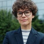 Portrait of a confident woman in business attire with curly hair and glasses outdoors.