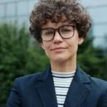 Portrait of a confident woman in business attire with curly hair and glasses outdoors.